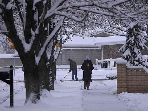 A man clears his driveway of snow as a woman walks down the sidewalk after an overnight storm in Provo,Utah on December 13, 2022.