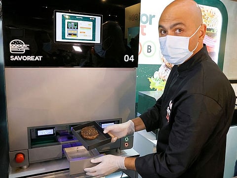 A man extracts a cooked plant-based hamburger with a meaty taste, produced by a robot according to customer requirements, to be offered in a sandwich by Israeli fast food brand BBB in the Israeli coastal town of Herzliya.