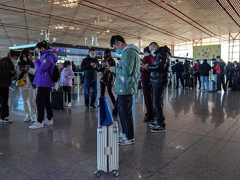 Masked travellers use their smartphones to fill in their health declaration after checking in at the international flight check in counter at the Beijing Capital International Airport in Beijing, Thursday, Dec. 29, 2022.