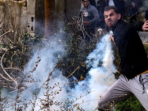 A Palestinian demonstrator returns a tear gas canister fired by Israeli troops during confrontations with them following a protest against the expropriation of Palestinian land by Israel in the West Bank village of Kfar Qaddum on January 6, 2023.