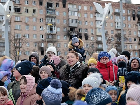Local citizens watch a performance near a Christmas tree decorated for Orthodox Christmas and the New Year festivities in Mariupol, in Donetsk region, eastern Ukraine, on January 5, 2023.