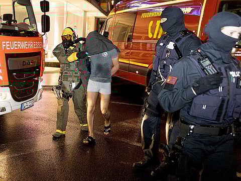 A man (2L) is led away following his arrest by a Special Task Force (SEK) police officer wearing protective gear in Castrop-Rauxel, western Germany on January 8, 2023 on suspicion of preparing an 'Islamist attack' using cyanide and ricin.