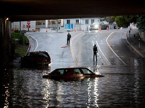 People photograph a car sitting in flooded water at an underpass in Oakland, California.
