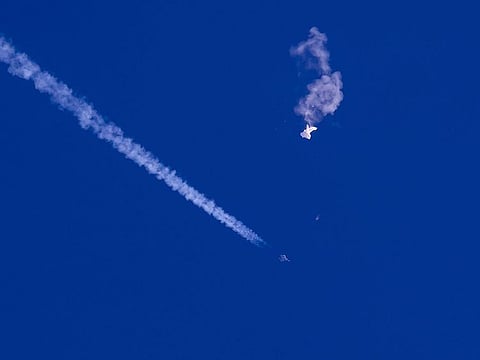 In this photo provided by Chad Fish, the remnants of a large balloon drift above the Atlantic Ocean, just off the coast of South Carolina, with a fighter jet and its contrail seen below it, Saturday, Feb. 4, 2023.