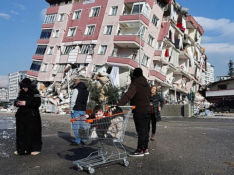 Children sit in a shopping cart near a collapsed building following an earthquake in Hatay, Turkey, February 7, 2023.