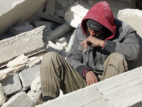 A Syrian man sits amidst the rubble as he waits for new about family members stuck under the wreckage in the town of Harim in Syria on the border with Turkey, on February 8, 2023.