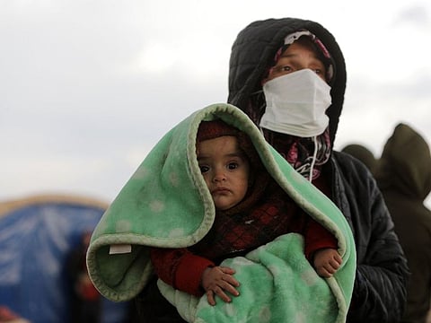 A woman carrying a baby watches as search and rescue operations continue days after a deadly earthquake hit Turkey and Syria, in the town of Jindayris in Aleppo.