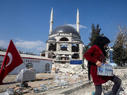 A girl carries a box of water bottles next to a damaged mosque in the aftermath of a deadly earthquake in Antakya, Turkey, on February 16, 2023.