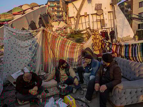 Men sit in front of the rubble of an area destroyed during the earthquake in Antakya. Some of the people waiting hope for a miracle.