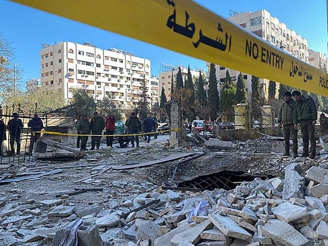 Police officers stand on the rubble of a damaged building at the site of a rocket attack, in central Damascus' Kafr Sousa neighbourhood. Illustrative image.