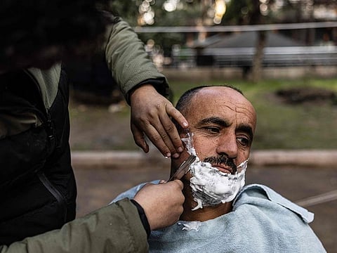 Syrian Khaled Al Hamo is having a hair cut by his 18-year-old son Mohammed, in front of his tent at a makeshift camp in the city of Antakya.
