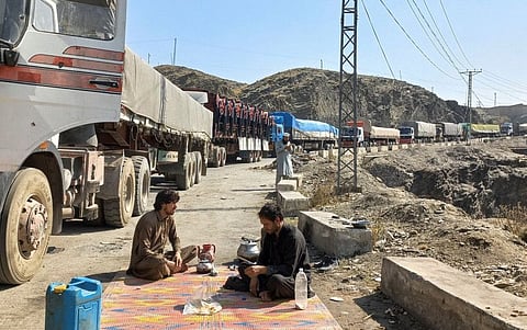 Men sit near a queue of trucks loaded with supplies to leave for Afghanistan, after Taliban authorities have closed the main border crossing in Torkham, Pakistan, on February 21, 2023.