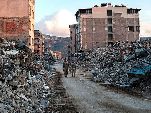 Turkish Army's UN forces walk amomg collapsed buildings, a day after a 6.4-magnitude earthquake struck the region, in the coastal city of Samandag on February 21, 2023.
