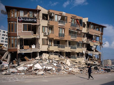 A pedestrian walks past a destroyed residential building in Hatay, Turkey.
