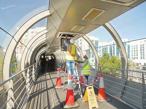 Workers do maintenance work at an air-conditioned glazed footbridge in Dubai.