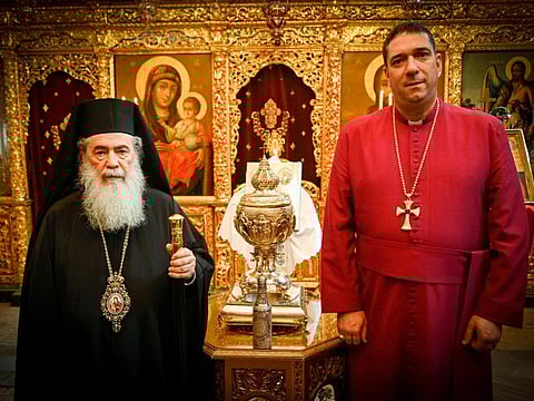 A handout picture taken and released on March 3, 2023 by Patriarchate of Jerusalem and Buckingham Palace shows the Patriarch of Jerusalem, His Beatitude Patriarch Theophilos III (left) and the Most Reverend Dr Hosam Elias Naoum, the Anglican Archbishop in Jerusalem, poses for a photograph with the the silver urn containing the Chrism Oil, made from oil from the mount of olives mixed with essential oils, which will be used in the Coronation of King Charles III.