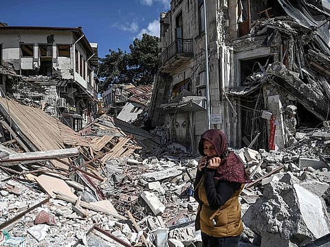A woman stands among the rubble of collapsed buildings in Hatay on March 6, 2023, one month after a massive earthquake struck southeastern Turkey.