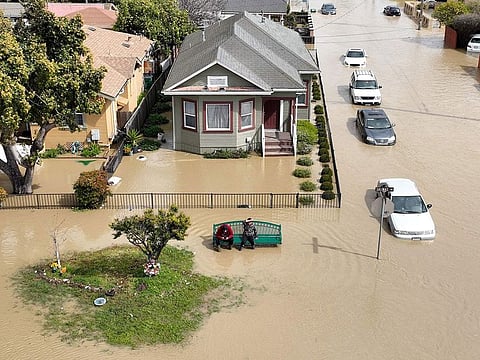 An aerial view shows people sitting on a bench in a flooded neighborhood in the unincorporated community of Pajaro in Watsonville, California on March 11, 2023.