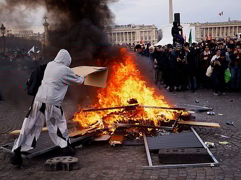 A protester throws a cardboard to feed burning pallets during a demonstration at Concorde square near the National Assembly in Paris.