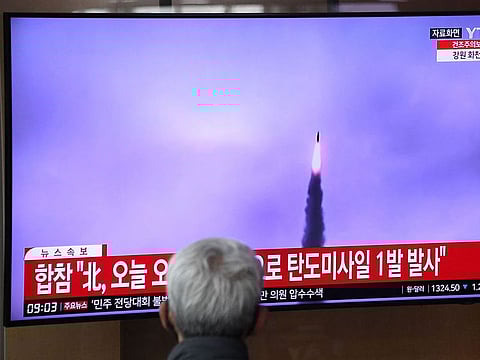 A man watches a television screen showing a news broadcast with file footage of a North Korean missile test.