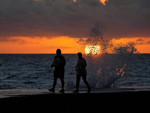 The sun rises above the Atlantic Ocean as waves crash near beach goers walking along a jetty, Dec. 7, 2022, in Bal Harbour, US.