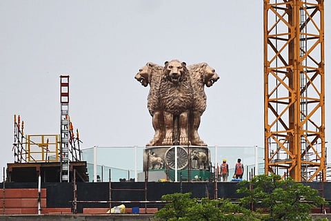 In this file photo taken on July 12, 2022, workers stand next to the newly inaugurated 'National Emblem' installed on the roof of the new Indian parliament building in New Delhi.