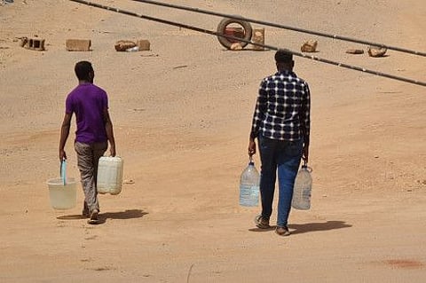 Sudanese men carry bottles of water back to their home in Khartoum on May 25, 2023.