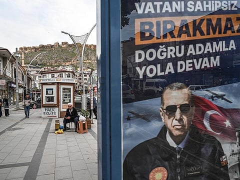 People sit next to a election banner of Turkish President at Bayburt city centre, north-east Turkey, on May 23, 2023.