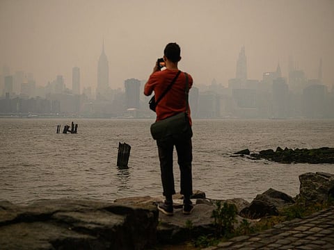 A man stands before the New York city skyline and east river shrouded in smoke, in Brooklyn on June 6, 2023.
