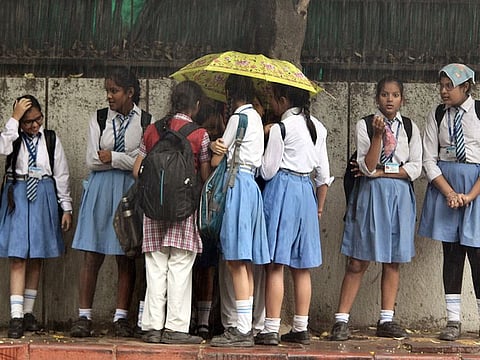 Children waiting for school bus under umbrellas in New Delhi, India