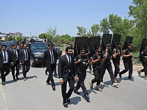 Security personnel with ballistic shields escort a vehicle carrying Pakistan's former Prime Minister Imran Khan, as he arrives to appear before the court in Islamabad on June 19, 2023.