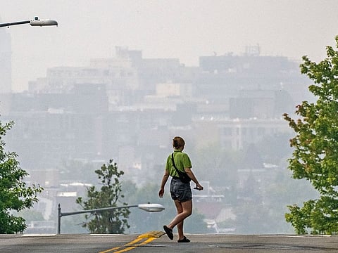 A woman crosses a street as smoke from the Canadian wildfires renders the cityscape amorphous in Washington, DC.
