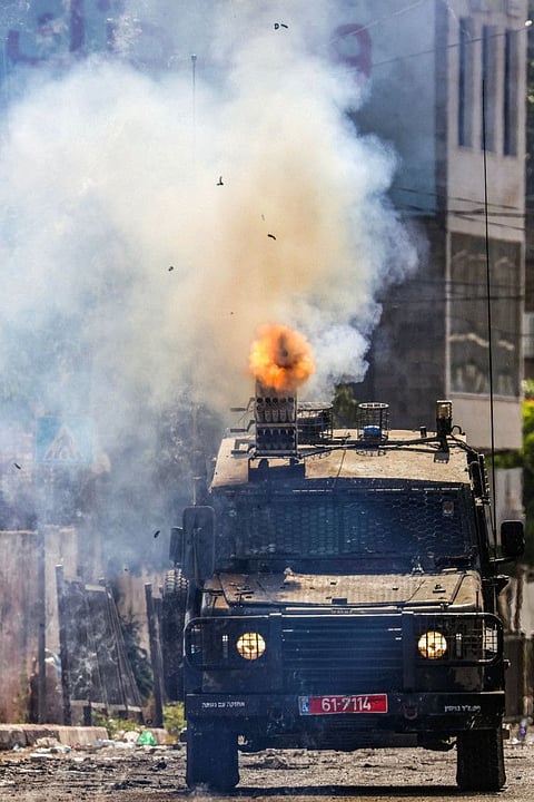 Israeli soldiers fire tear gas canisters from an armoured vehicle during an ongoing military operation in the West Bank city of Jenin on July 4, 2023.