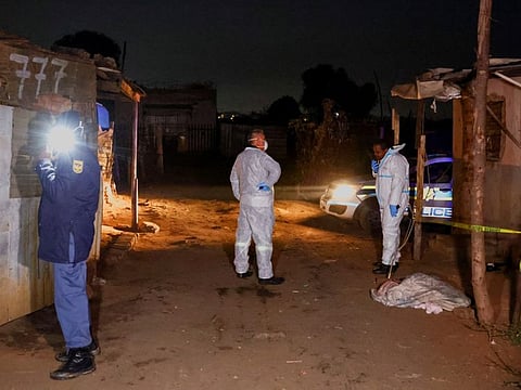 A police officer and forensic team members stand near the body of a child covered by a piece of cloth at the scene of a suspected gas leak thought to be linked to illegal mining, in the Angelo shack settlement, near Boksburg, east of Johannesburg, South Africa July 6, 2023.