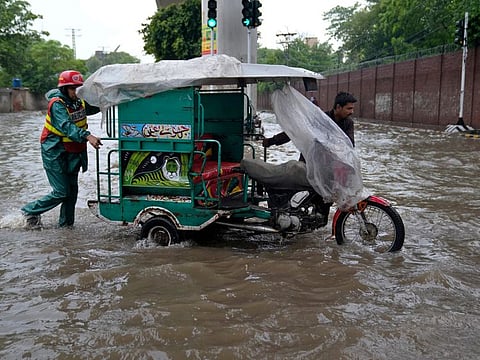 A rescue worker helps a driver pushing his motorcycle rickshaw through a flooded road caused by heavy monsoon rainfall in Lahore.