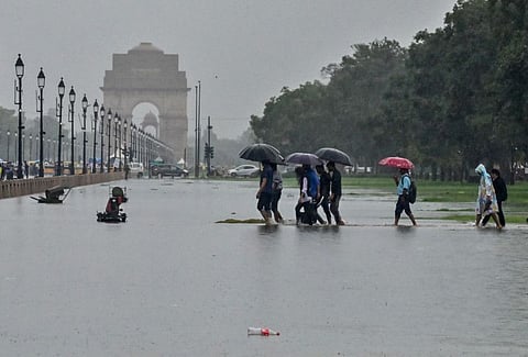 People cover their heads with umbrellas as they wade through waterlogged streets at India Gate during heavy rainfall, in New Delhi on Sunday, July 9, 2023.