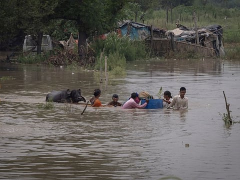 Residents carry their belongings through a field flooded with the rising water level of river Yamuna after heavy monsoon rains in New Delhi on July 11, 2023.