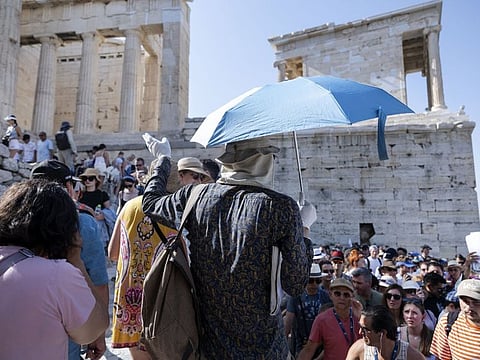 A tour guide uses an umbrella and gloves to shield himself from the sun with while touring the Acropolis archaeological site, during extreme hot weather conditions, in Athens, Greece, on July 14, 2023.