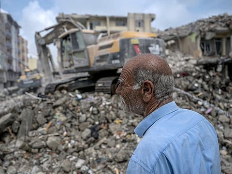 A man watches as diggers work to clean the rubble of collapsed buildings, five months after a 7.8-magnitude jolt and its aftershocks wiped out swathes of Turkey's mountainous southeast, in Samandag on July 9, 2023.