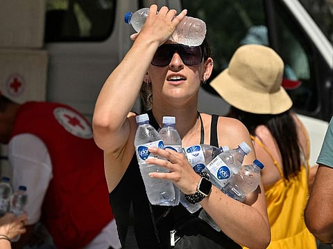 A woman cools off with cold bottles of water, distributed by the hellenic red cross organization near the entrance of the Acropolis archeological site in Athens.