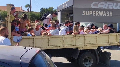 Tourists sit in the back of an open air lorry as they are evacuated during wildfires on the Greek island of Rhodes.