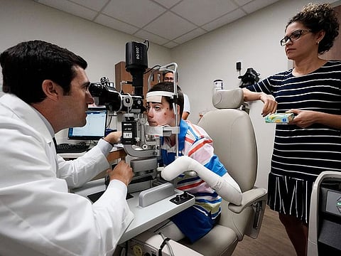 Dr. Alfonso Sabater, left, examines Antonio Vento Carvajal's eyes accompanied by his mother, Yunielkys Carvajal, right, at University of Miami Health System's Bascom Palmer Eye Institute in Miami.