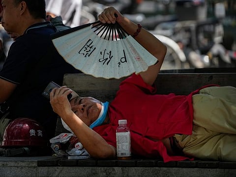 A man cools himself with a fan while browsing his phone on a sweltering day in Beijing on July 16, 2023.
