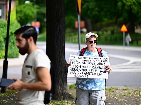 A woman with a protest poster stands next to Ahmad A. (left) who has been given permission by the police for a public gathering to burn a Torah and a Bible outside the Israeli embassy in Stockholm, Sweden, on July 15, 2023.
