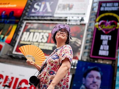 A tour guide fans herself while working in Times Square as temperatures rise, in New York. Nearly 60% of the US population, are under a heat advisory or flood warning or watch as the high temperatures spread and new areas are told to expect severe storms.