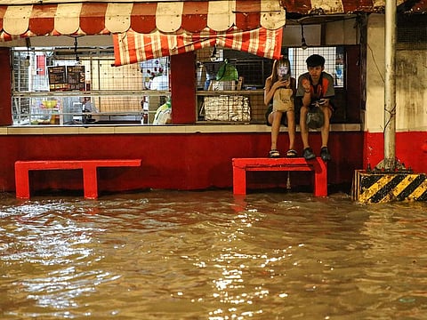 People wait for transportation along a flooded street of Manila as typhoon Khanun intensifies the southwest monsoon rain.