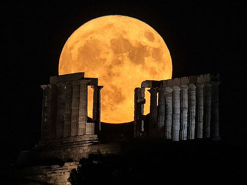 The full moon rises behind the ancient temple of Poseidon at cape Sounion, south of Athens on August 1, 2023.