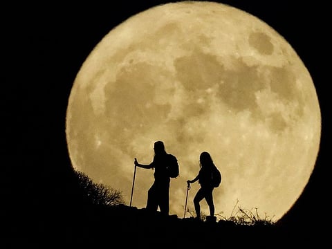 Women walk up a mountain with the full moon known as the 'Sturgeon Moon' in the background, in Arguineguin, in the island of Gran Canaria, Spain, August 1, 2023.