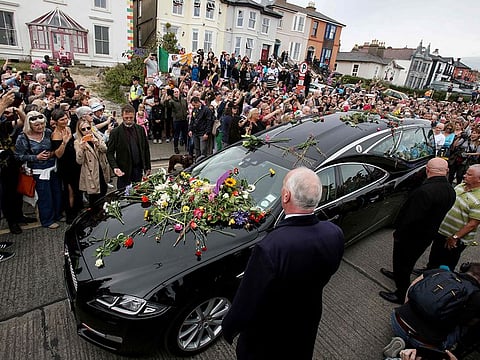 People lay flowers and tributes on the hearse during the funeral procession of late Irish singer Sinead O'Connor, outside the former home in Bray, eastern Ireland, ahead of her funeral on August 8, 2023.