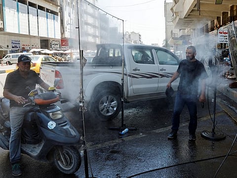 Iraqi men stand in front of water mist amid an ongoing heatwave, in Baghdad, on August 6, 2023.